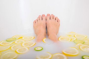 Obraz na płótnie Canvas Girl takes a milk bath with lemons and limes. Citrus spa. Body care. Skin whitening. Women's legs.