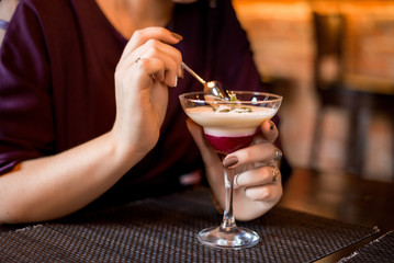 In a restaurant, women's hands hold a dessert in a glass bowl