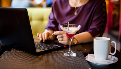 In the cafe, work with a laptop and drink coffee. Women's hands check the phone. Remote work of a freelancer