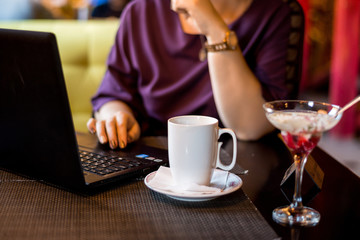 In the cafe, work with a laptop and drink coffee. Women's hands check the phone. Remote work of a freelancer