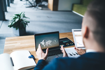 Crop businessman watching world map and tablet with assistant