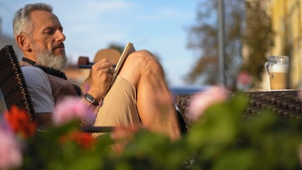 Successful writer enthusiastically takes notes relaxing on a sunny morning in a cafe