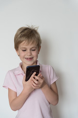 Fototapeta premium A cute child is laughing loudly, holding a cell phone in his hand.