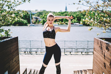 Elastic sportswoman straining hands at quay on sunny day