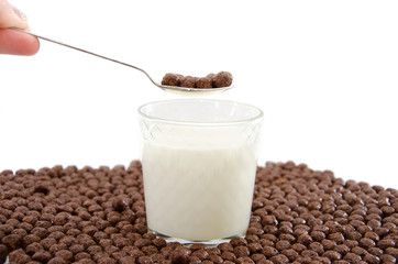 glass of milk, spoon in hand and chocolate balls on a white. Cereal.