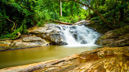 Beautiful waterfall Mae Sa, Thailand. Fresh and pure water stream is flowing on the rock stone ground in tropical rainforest. Fresh plants and trees above river. Vibrant colors in pure nature