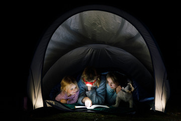 Obraz na płótnie Canvas Girls reading a book with torch at night during summer holidays