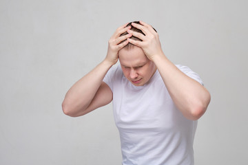 A man in a white T-shirt suffers from headaches and migraines.