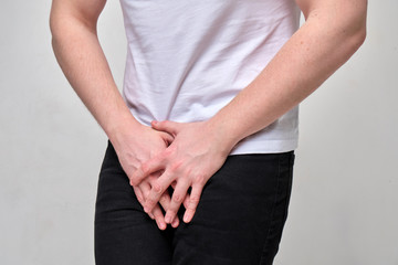A man in a white T-shirt suffers groin pain. The problem with urology.