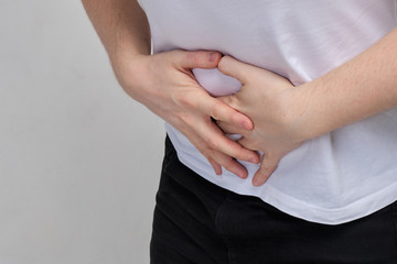A man in a white T-shirt clutched at his stomach in pain. Food poisoning concept.