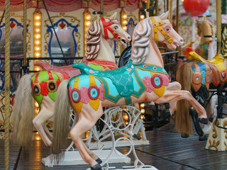 Fototapeta na wymiar Colorful vintage merry-go-round wooden horses. Photography of the city amusement park. Downtown buildings as background. Concepts of fun and childhood.