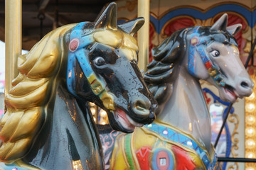 Fototapeta na wymiar Colorful vintage merry-go-round wooden horses. Photography of the city amusement park. Downtown buildings as background. Concepts of fun and childhood.