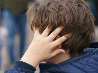 Fototapeta premium A boy in thought wrapped his arms around his head. He has a trendy youth hairstyle. Photography with defocused background.