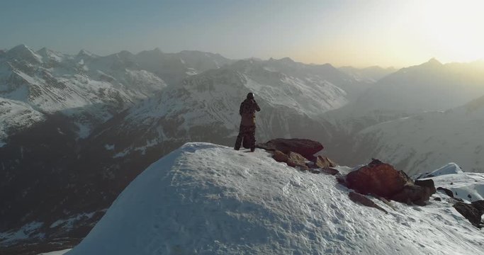 AEIRAL DRONE snowboarder enjoying the view from a mountain top early in the morning, preparing for freeride snowboarding. 4K UHD