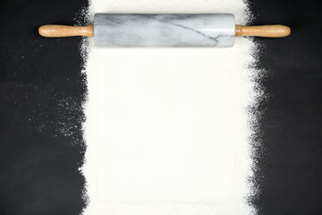 Flour and rolling pin on black table, flat lay