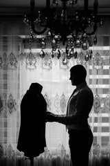 Black and white photo. The groom stands near a mannequin with a jacket. The groom is dressed at home. Cute groom posing for a photographer