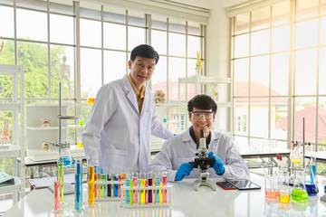 Two smiling asian professional senior and young doctor scientist using microscope and research in working laboratory.