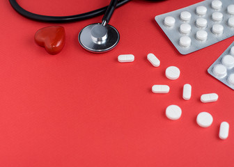 Medicine pills, capsules and stethoscope on a red background. Medicine concept. Copy space