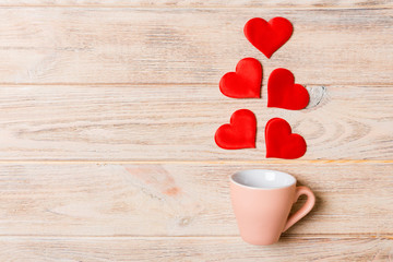Top view of a cup and red hearts falling out from it on wooden background. Happy Valentine's Day concept