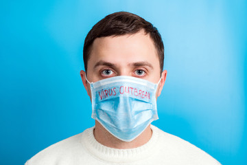 Portrait of young man wearing medical mask with virus outbreak word at blue background. Coronavirus concept. Respiratory protection