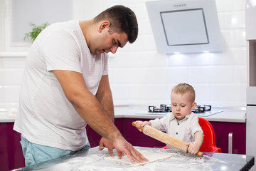 Obraz premium Kid rolls out the pizza dough. Happy family in kitchen.