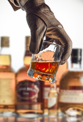 A hand in a leather glove raises a glass of alcohol from a bar counter