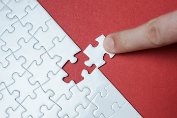 Hand putting piece of white jigsaw puzzle on red background. Team business success partnership or teamwork.