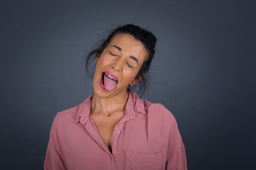 Obraz premium Beautiful caucasian woman with happy and funny face smiling and showing tongue. Wearing casual clothes and standing against gray studio background.