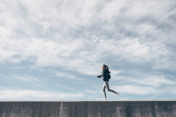 sports girl runs on a concrete wall against the sky