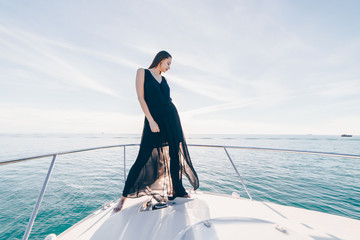 Naklejka premium lovely woman on board a yacht in a black evening dress stands aft on the background of the ocean