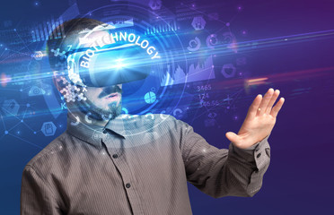 Businessman looking through Virtual Reality glasses with BIOTECHNOLOGY inscription, innovative technology concept