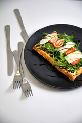 fried waffle with chicken, herbs, tomatoes, cheese, balsamic vinegar on a black plate