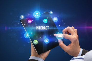 Businessman holding a foldable smartphone with INTERACT inscription, social media concept