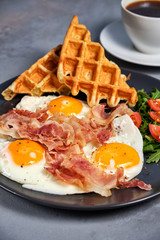 Hearty breakfast of scrambled eggs with bacon, waffles, a salad of greens and tomatoes and a cup of aromatic black coffee