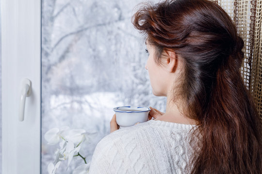 Woman With Cup In Hand Looking Out The Window .