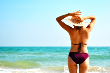 Woman in hat on the beach. Girl in a swimsuit in the ocean. Tropical summer vacation