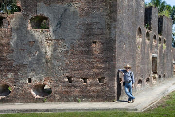 Old fortress brick wall of Fort Zeelandia on a clear Sunny day and a standing man in a cowboy hat, Guyana. World tourism, attractions, fortress.