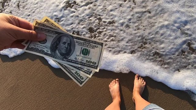 Girl holding money bill of 300 dollars on background of sea ocean waves
