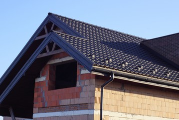 part of an unfinished house with a brown brick attic and an empty window under a tiled roof against a blue sky