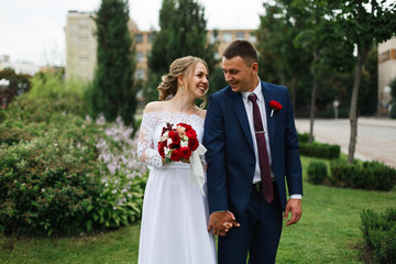 Portrait of beautiful wedding couple in love outdoors on building background. Happy newlyweds walking on city street in sunny day. Wedding day. smiling bride and groom holding hands on city street .
