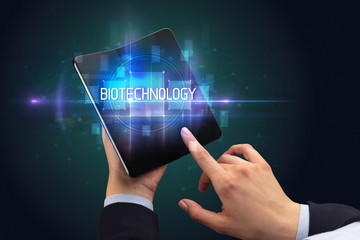 Businessman holding a foldable smartphone with BIOTECHNOLOGY inscription, new technology concept