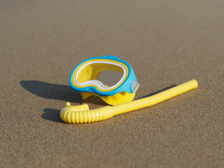 Yellow diving mask and snorkel on the beach sand. Top view.