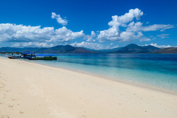 Two boats anchored to white sand beach on an island near Maumere, Indonesia. There is a fishing cottage on the side. Clear, turquoise coloured water displaying coral reef