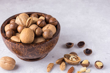 Different types of nuts - walnuts, almonds, macadamia in a bowl of coconut on a gray background.