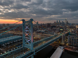 Philadelphia at night, aerial view of skzline at sunset with Benjamin Franklin Bridge and waterfront, skyscrapers dominating cityline against dramatic sky