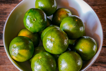 Oranges in white bowl on rustic wooden table. Asian local oranges.