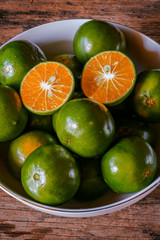 Two slices of oranges in white bowl and some others on rustic wooden table. Asian local oranges.