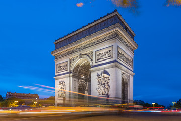 Fototapeta na wymiar Arc de Triomphe at dusk in Paris in France with traffic of cars light trails and yellow leafs moved by the wind