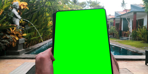 Man holding a tablet outside the pool while on vacation.