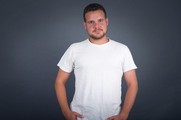 Young handsome man wearing white T-shirt over isolated background happy face smiling with hands in pockets looking at the camera. Positive person.